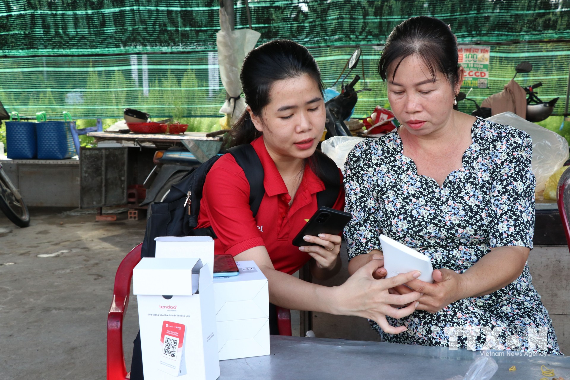 Hướng dẫn tiểu thương chợ Cầu Xây, xã Song Lộc, tỉnh Vĩnh Long, sử dụng bảng mã QR. (Ảnh: Thanh Hòa/TTXVN)